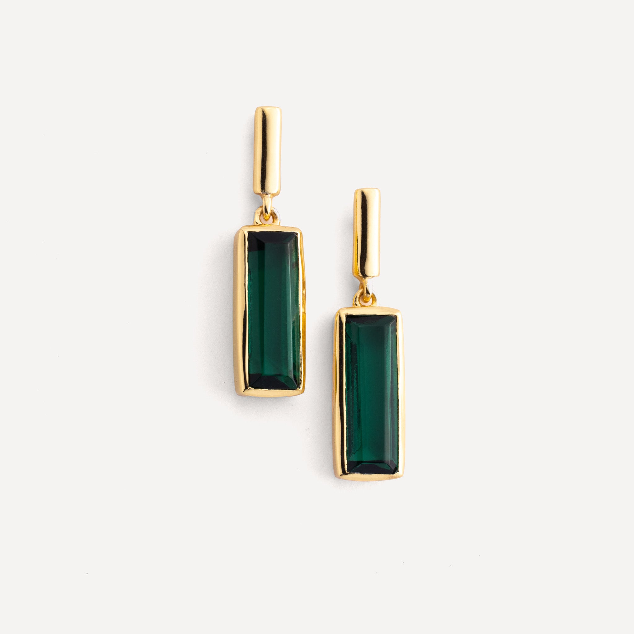 Gold earrings with green gemstones on a white background